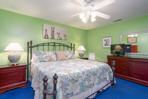 Un dormitorio con cama, mesitas de noche, cómoda, ventilador de techo y decoración en las paredes.