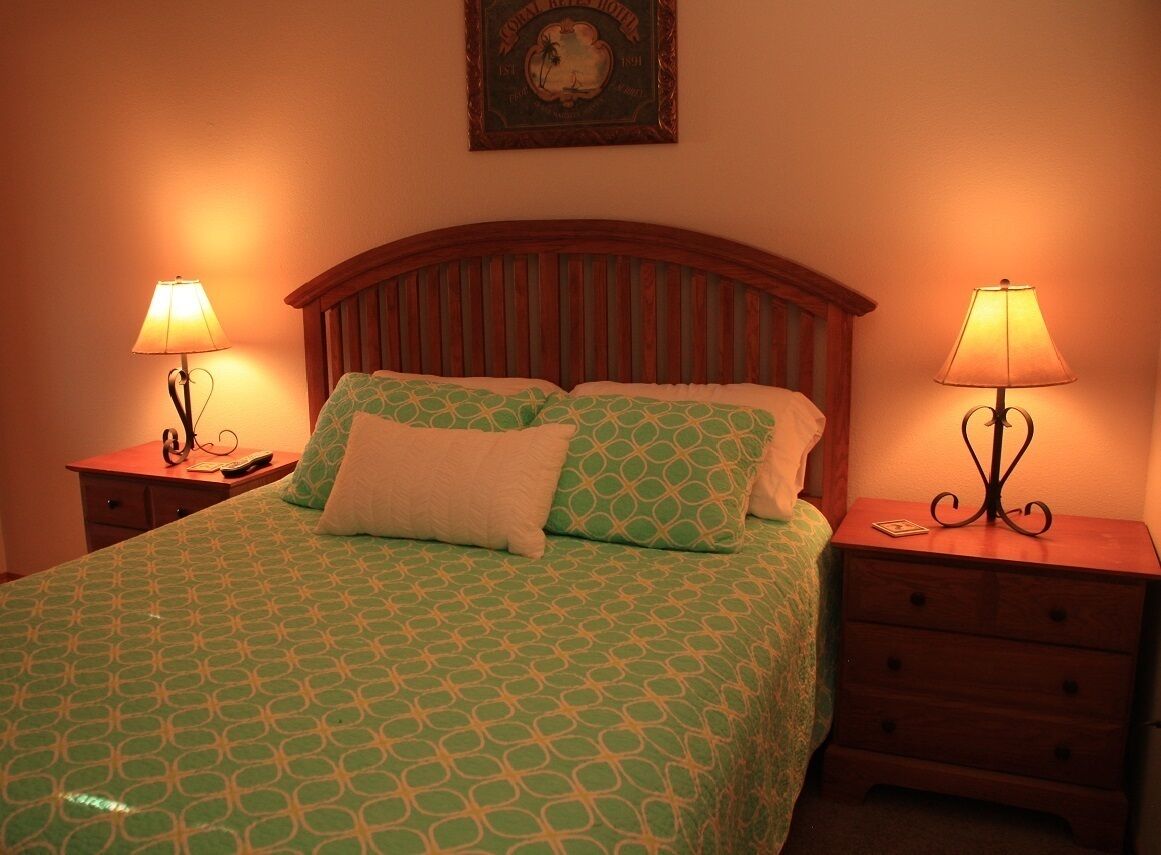 Una cama bien tendida con ropa de cama estampada, dos lámparas de noche y un cabecero de madera.