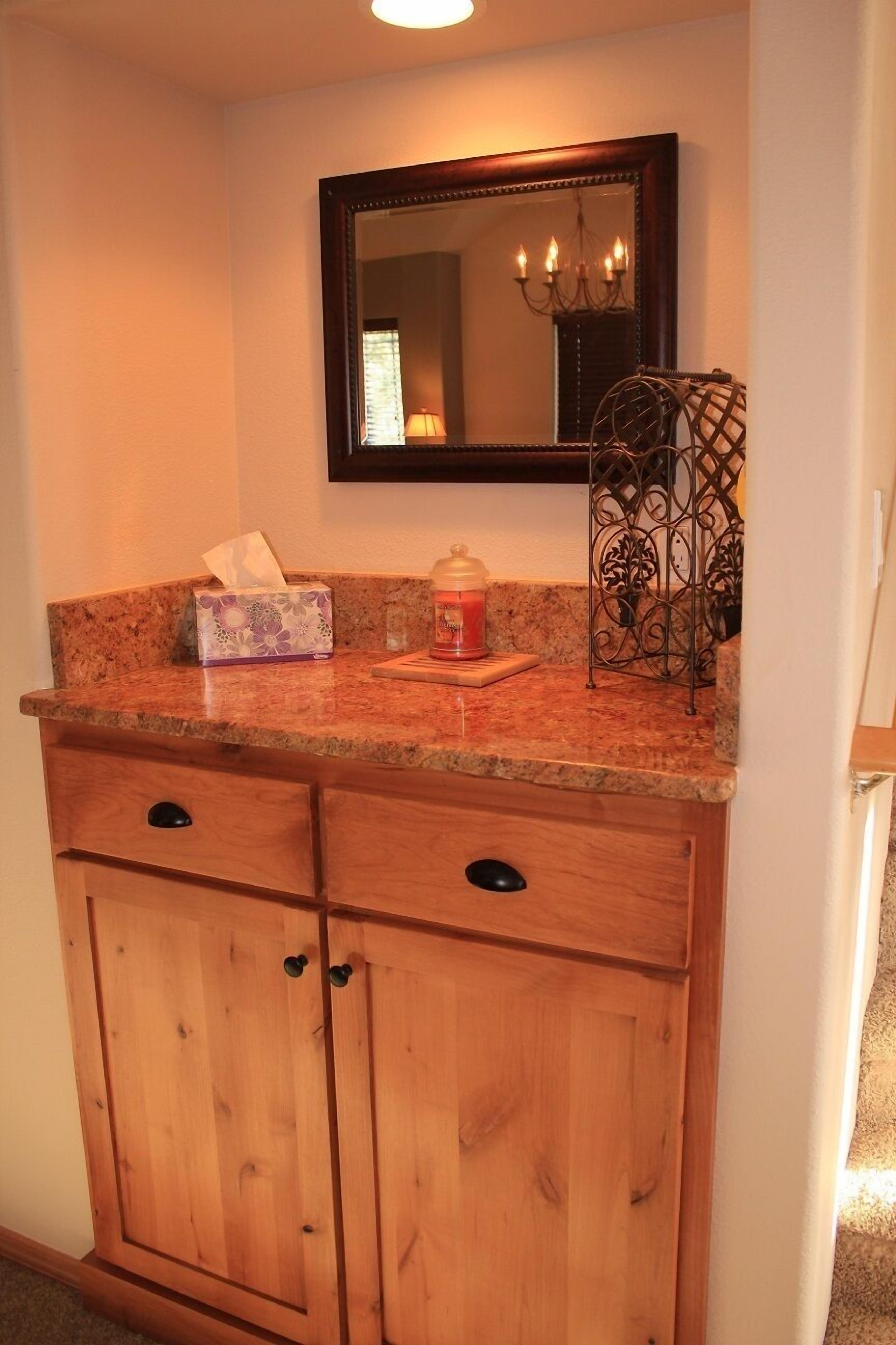 A bathroom vanity with a granite countertop, a wooden cabinet below, a mirror above, and a decorative metal rack.