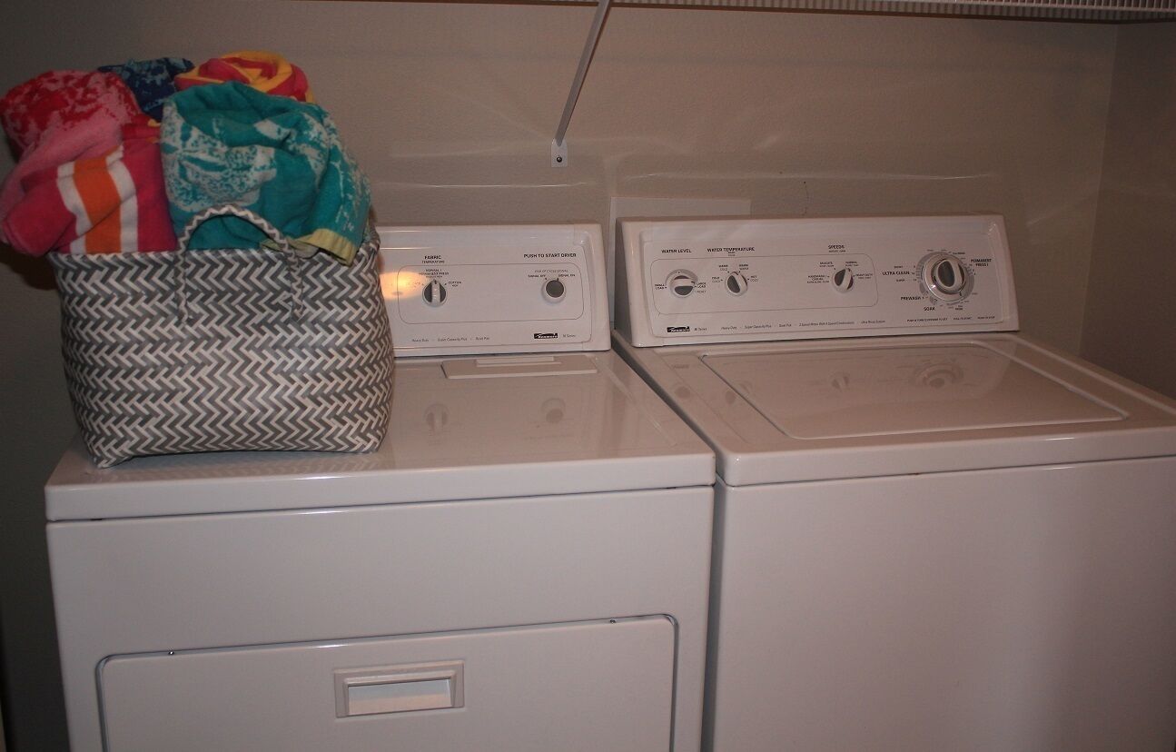 A front-loading washer and dryer unit with a basket of folded clothes on top.