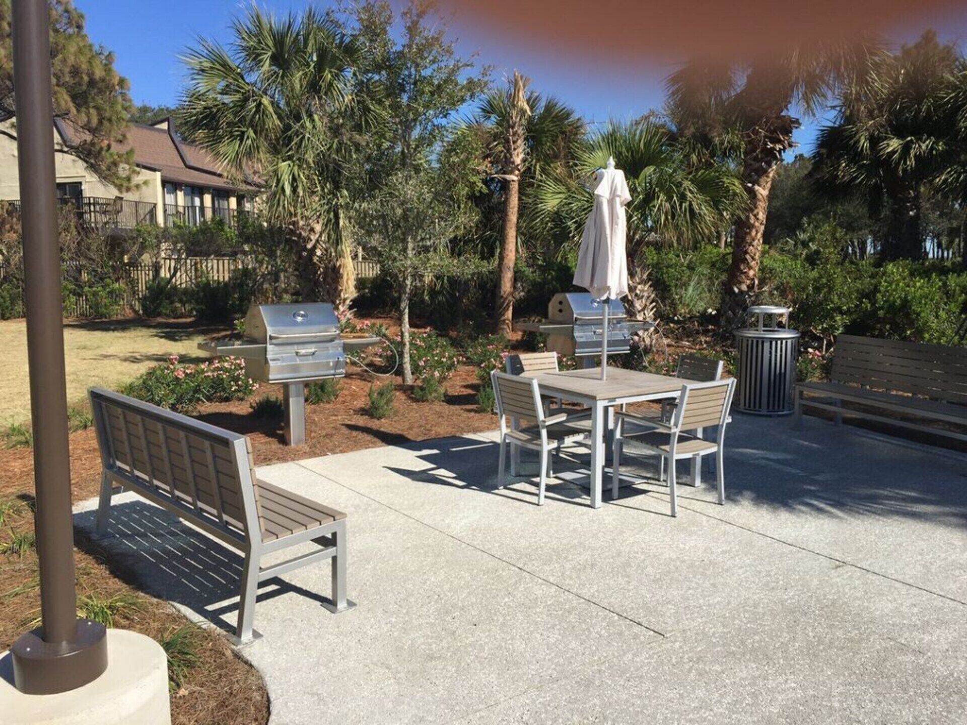 An outdoor patio with a table and chairs, a grill, and a bench.