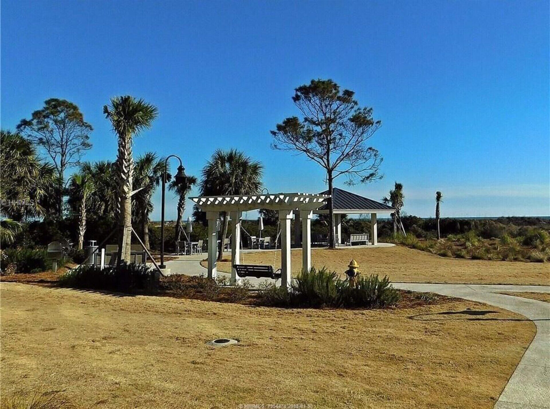 A gazebo with a patio, palm trees, and a building in the background.
