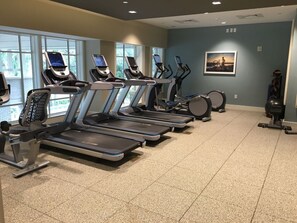 Une salle de sport équipée de tapis de course, de vélos elliptiques et d’un vélo d’appartement.