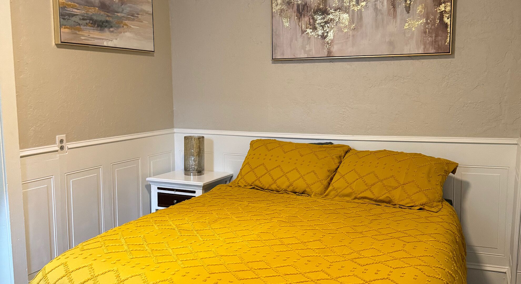 Una camera da letto con un letto, un comodino e due quadri appesi al muro.