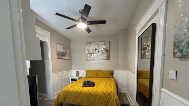 Une chambre à coucher avec un lit, un ventilateur de plafond et des œuvres d’art accrochées aux murs.
