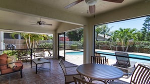 Un patio techado con piscina, mobiliario exterior y ventilador de techo.