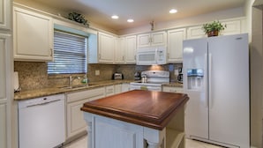 Una cocina con armarios blancos, encimera de granito, isla de madera, refrigerador y microondas.