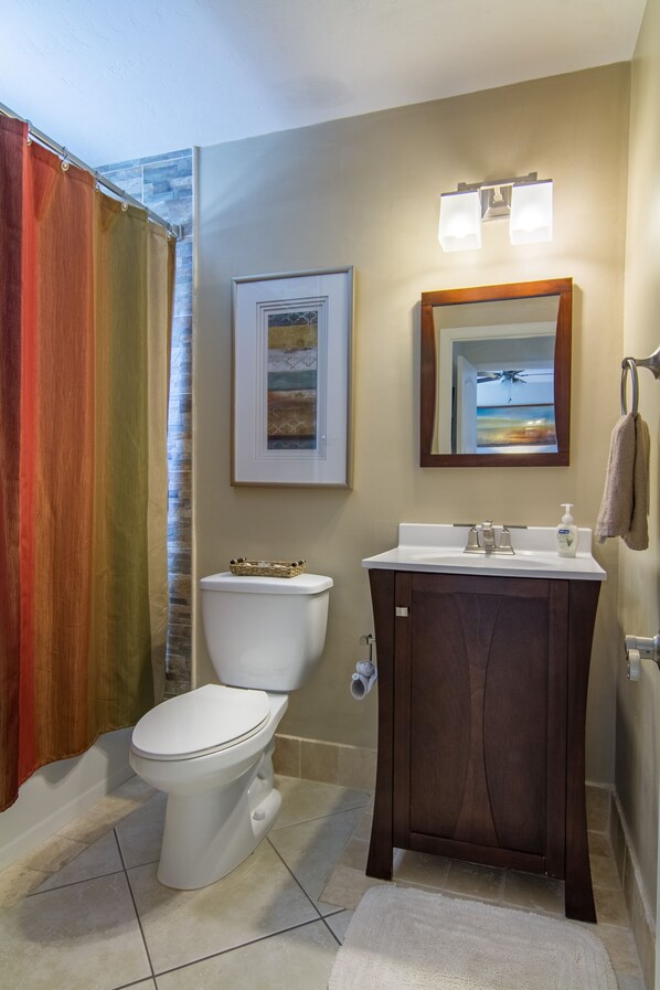 A bathroom with a white toilet, a dark wooden vanity, a framed picture on the wall, and a shower curtain. - Relax by the sand at nearby Vanderbilt Beach or hang by heated pool (Naples)