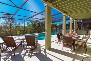 Um pátio externo com piscina, área de estar coberta e mesa de jantar para dois.