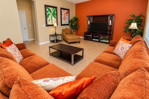 A living room with orange sofas, a coffee table, a TV, and two framed pictures on the wall.