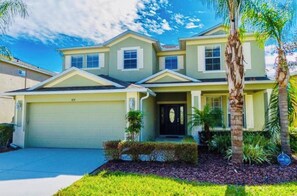 A two-story residential house with a garage, a front porch, and a well-maintained lawn with palm trees.