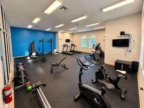 A gym with various exercise equipment, a fire extinguisher, and a television on the wall.