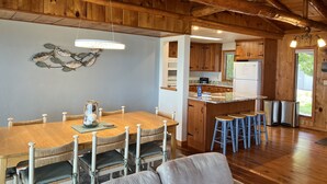 Eine geräumige Küche mit Holzausbau, einer zentralen Kochinsel mit Barhocker und einem Essbereich mit Holztisch und Stühlen.
