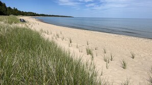 Ein Strand mit blauem Himmel, sandigem Ufer und einigen Grashalmen.