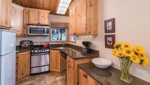 A kitchen with wooden cabinets, a stainless steel stove, a microwave, and a sink. There is a vase with sunflowers on the counter.