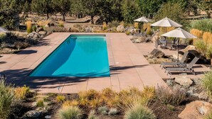 A rectangular swimming pool with a clear blue water, surrounded by a patio area with lounge chairs and umbrellas.