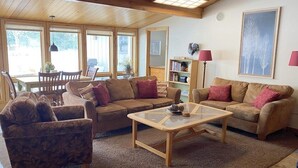 A cozy living room with wooden ceilings, a glass coffee table, and two sofas with cushions.