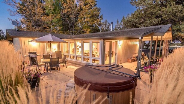A wooden cabin with a hot tub, patio furniture, and a covered outdoor area with a grill.