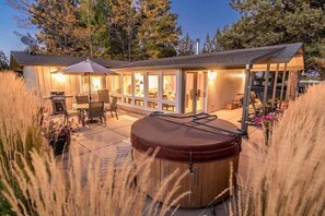 A wooden cabin with a hot tub, patio furniture, and a covered outdoor area with a grill.