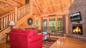 Un interior de madera con un sofá rojo, una chimenea, un televisor montado en una pared de piedra y una escalera.