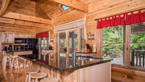 Interior de una cabaña de madera con una zona de cocina que incluye una barra, taburetes y un lavabo.