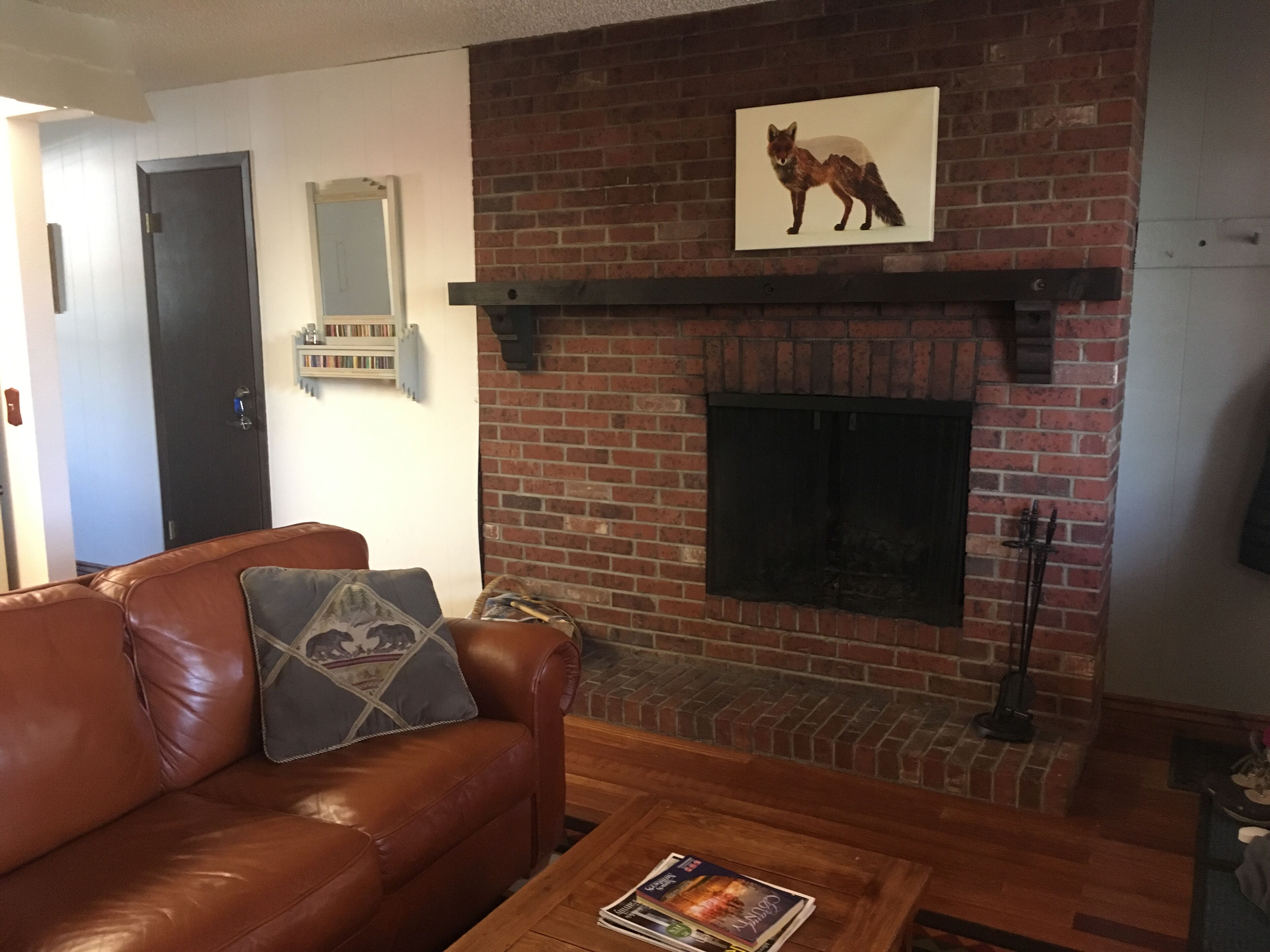 Una sala de estar con chimenea de ladrillo, un sofá de cuero marrón y una mesa de centro con una revista.