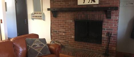 Una sala de estar con chimenea de ladrillo, un sofá de cuero marrón y una mesa de centro con una revista.