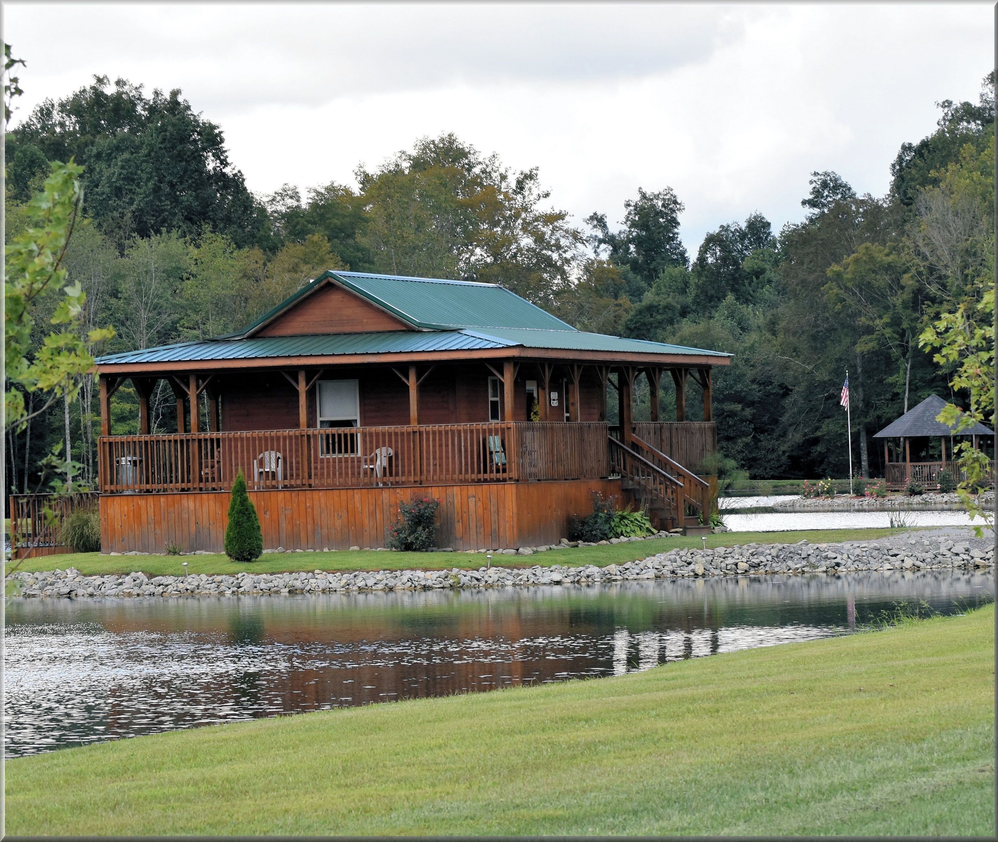 A wooden lodge with a porch, a small deck, and a pond in front.