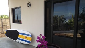 Una tabla de surf apoyada contra una pared, un vidrio y una silla con un florero.