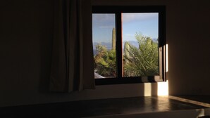 Una habitación con ventana que da a un paisaje desértico, con cactus y palmeras.
