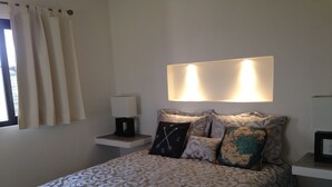 Un dormitorio ordenado con una colcha estampada, una lámpara de noche y almohadones decorativos que incluyen una brújula y un mapa.
