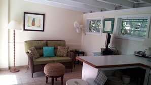 A cozy living room with a sofa, a small round table, a fan, and a kitchen area with a counter and shelves. -  Cute Cozy Cottage with private entrance and ocean views in prime neighborhood (St. John)