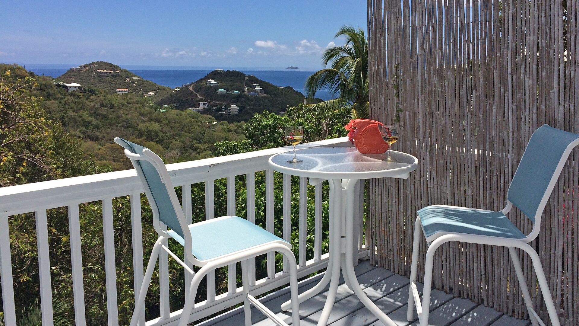 Een balkon met twee stoelen en een tafel, met uitzicht op een schilderachtig landschap van heuvels en de oceaan.