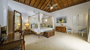 Une chambre spacieuse avec un lit à baldaquin, un ventilateur de plafond et un grand tableau accroché au mur.
