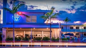 Un hôtel avec une enseigne au néon, des palmiers et un ciel au coucher du soleil.