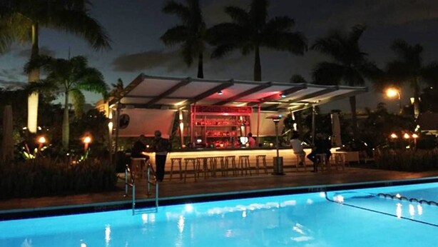 Un espace bar situé au bord de la piscine, avec une piscine, des palmiers et un coin salon abrité.