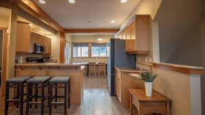 A modern kitchen with wooden cabinets, a central island with bar stools, and a refrigerator.