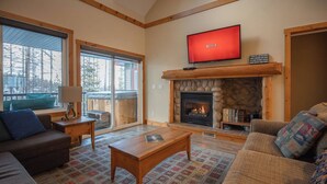 A cozy living room with a fireplace, a television, and a large window overlooking a snowy landscape.