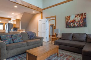 A spacious living area with a gray sofa, a brown sofa, and a wooden coffee table. A colorful abstract painting hangs on the wall. - KR410 by Simply Kimberley | Ski-In/Out + Private Hot Tub (Kimberley)