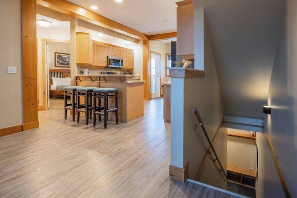 A modern kitchen with wooden cabinets, a central island with stools, and a built-in microwave. - KR410 by Simply Kimberley | Ski-In/Out + Private Hot Tub (Kimberley)