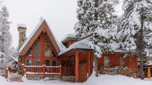 A log cabin with a stone chimney, wooden deck, and snow-covered surroundings.