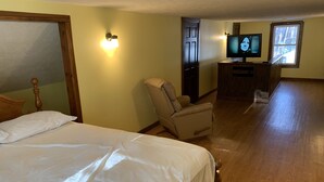 A hotel room with a bed, a chair, a desk with a TV, and a window.