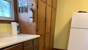 A kitchen with wooden cabinets, a white refrigerator, and a window with a view of trees.