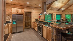 A modern kitchen with wooden cabinetry, stainless steel appliances, and a stone island. - Crystal Ridge, Wet Spa, Pool Table, Arcade Game, Hot Tub, Wood-burning Fireplace (Broken Bow)