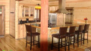 A wooden cabin interior with a kitchen, dining area, and a stone fireplace. - Crystal Ridge, Wet Spa, Pool Table, Arcade Game, Hot Tub, Wood-burning Fireplace (Broken Bow)