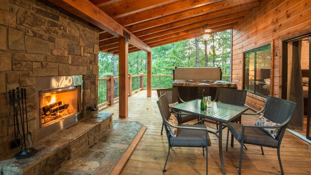 A covered outdoor patio with a stone fireplace, metal table, and chairs. - Crystal Ridge, Wet Spa, Pool Table, Arcade Game, Hot Tub, Wood-burning Fireplace (Broken Bow)