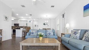 A spacious living room with a blue sofa, a wooden coffee table, and a kitchen in the background. - Canalside Retreat: 4Br, 3BA with Pool & Stunning Canal Views! (Marathon)
