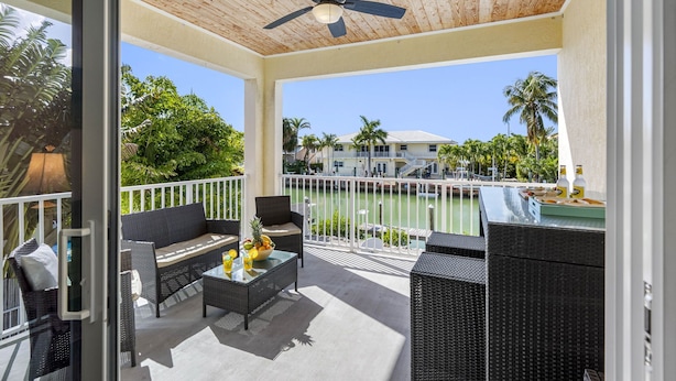 A covered outdoor area with wicker furniture, a ceiling fan, and a view of a marina. - Canalside Retreat: 4Br, 3BA with Pool & Stunning Canal Views! (Marathon)