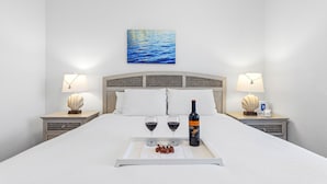A neatly made bed with a tray of wine, glasses, and grapes, two bedside lamps, and a painting of the sea on the wall. - Canalside Retreat: 4Br, 3BA with Pool & Stunning Canal Views! (Marathon)