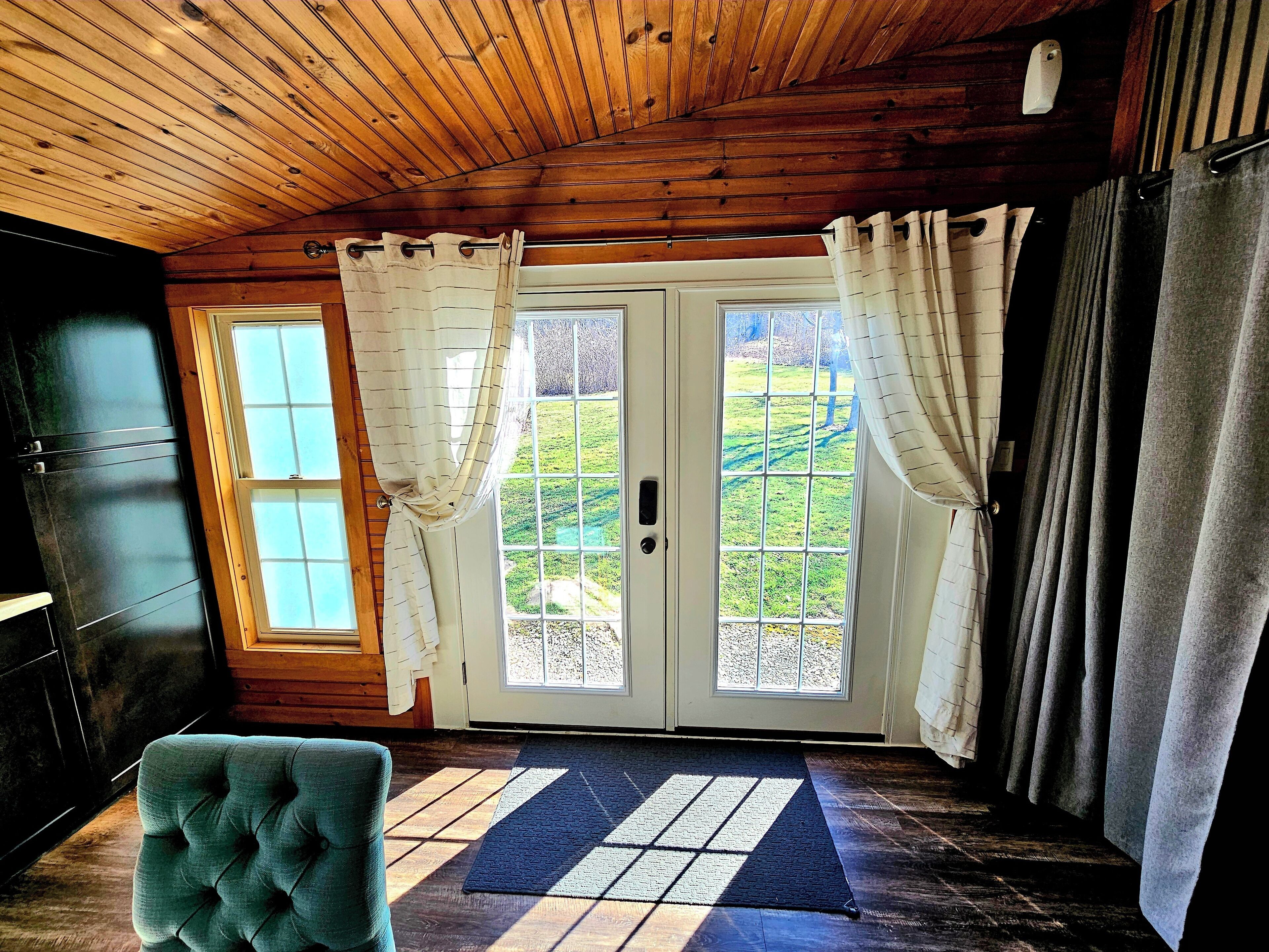 A room with a wooden ceiling, a door with glass panels, a blue rug, and a tufted chair.